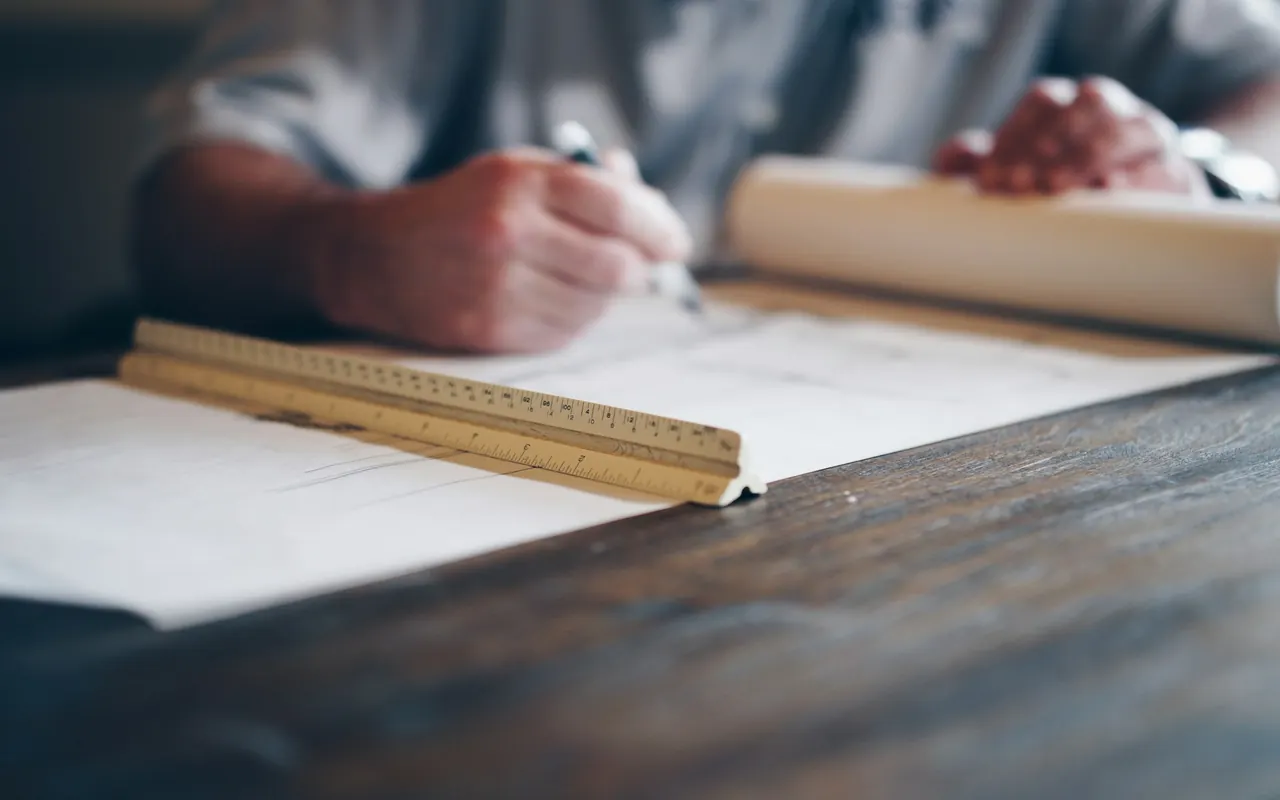 Hands marking up building plans with a pencil and a scale ruler