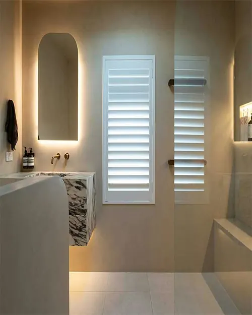 Ensuite with a backlit arched mirror, a stone vanity and plantation shutters