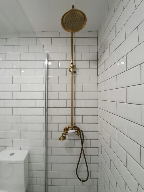 Shower lined in white subway tiles with an exposed brass rail shower