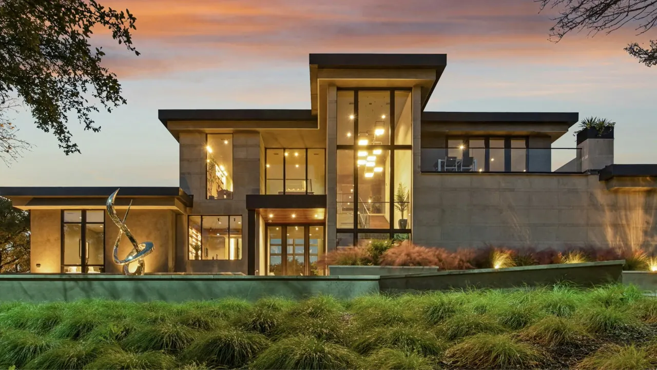 Modern two-storey home at dusk, warm light glowing through floor-to-ceiling glass