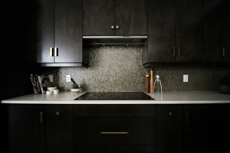 Kitchen with black joinery, brass handles and a mosaic tile splashback